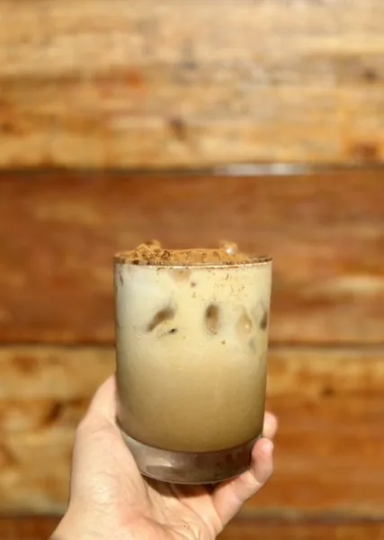 A hand holding an iced latte over the trailer's cedar planks