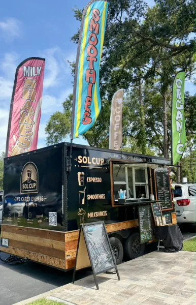The Sol Cup trailer set up at a market with tall feather flags reading milkshakes, smoothies, coffee and organic