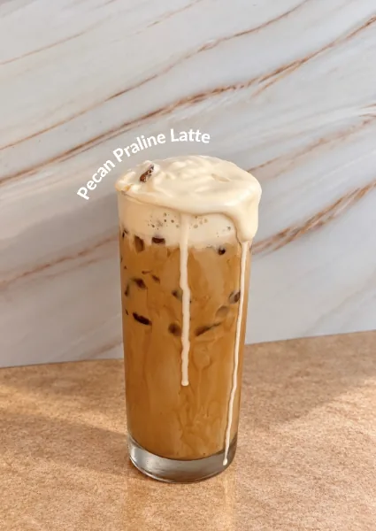 A tall iced pecan praline latte with a cream cold-foam top, against a marble background