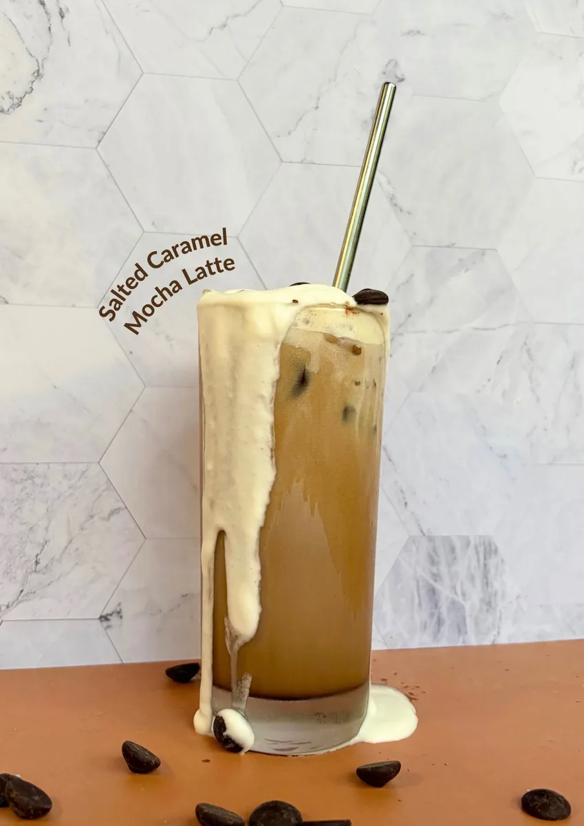 An iced salted caramel mocha latte with cold foam spilling over the rim and a metal straw