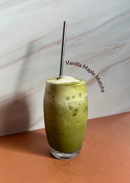 An iced vanilla maple matcha, bright green with a cream top, and a metal straw